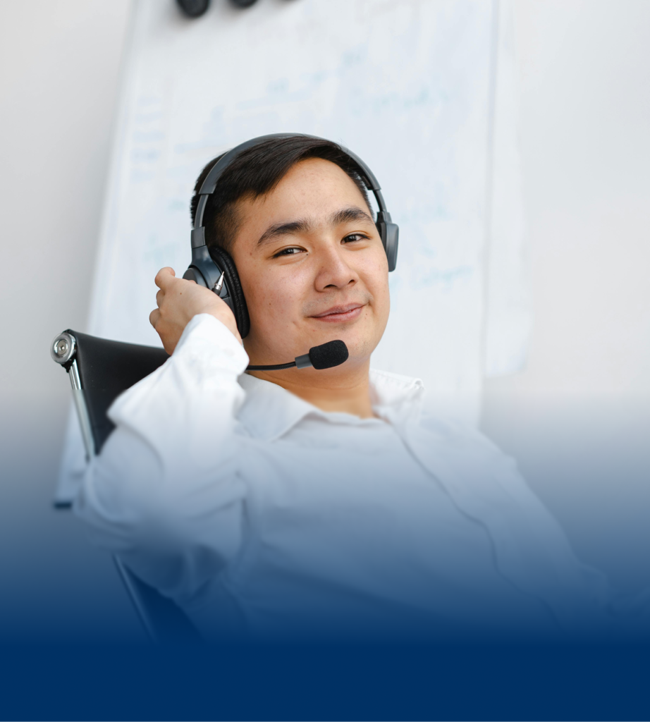 TSR-square-img Male call center agent wearing a headset, smiling calmly while adjusting the earpiece in a professional office environment